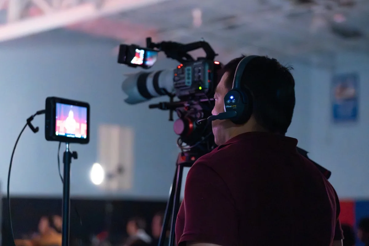 Camera operator with a headset filming a presentation at Harmony TEDx.